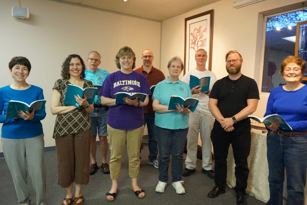 Image of the Channing Choir, 9 adults, in front of the room